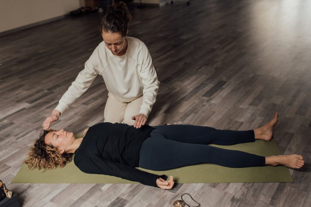 Energy therapist healing barefoot female with closed eyes during meditation practice on floor in sunlight